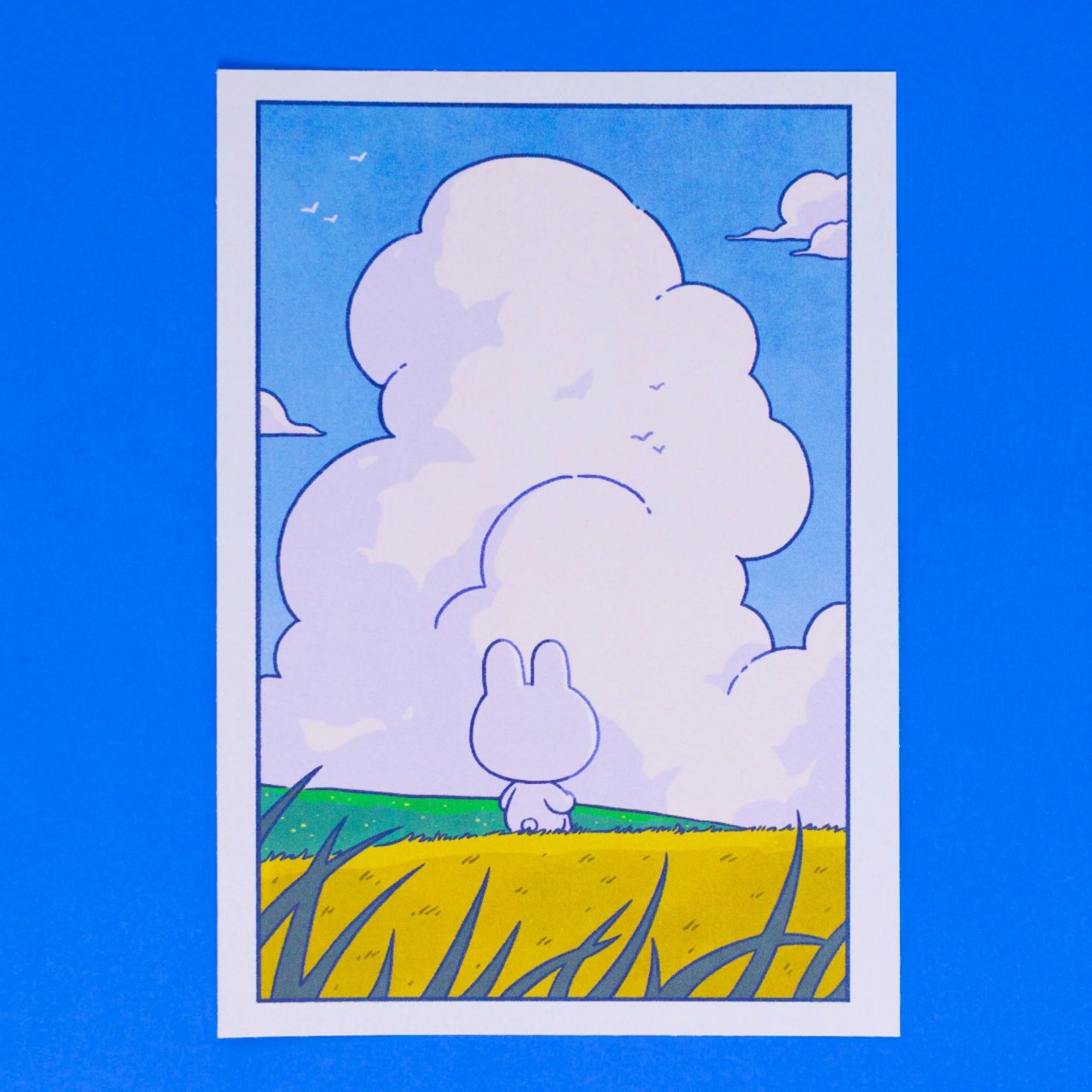 Art print showing the back of a bunny sitting in a field, looking at a big column of clouds.