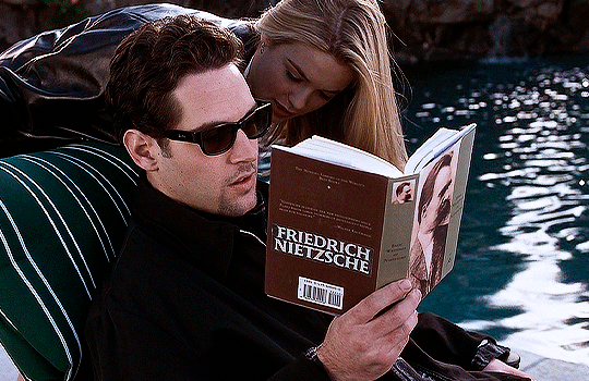 gif 10 of 10. Josh is wearing all black clothing and sunglasses. he's reading Nietzsche near the pool. Cher is bothering him by touching his cheek. end ID.