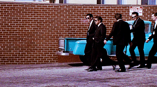 gifs from a scene of Reservoir Dogs (1992). 8 men are walking together, 6 of them wearing black suits and sunglasses. each actor is credited in their respective close ups. the scene ends with the main title appearing on screen as the group walk away from the camera. end ID.