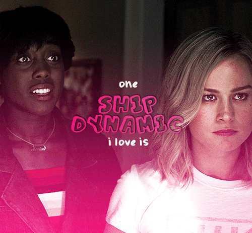 Gif #01 of 5. Gif of Maria Rambeau and Carol Danvers of the Marvel Cinematic Universe. Carol and Maria are standing next to each other, Maria with an awkward smile given to someone off screen while Carol is glaring at that same off screen person. The text says "one ship dynamic I love is". There's also an animation of a pink heart being drawn under the text.