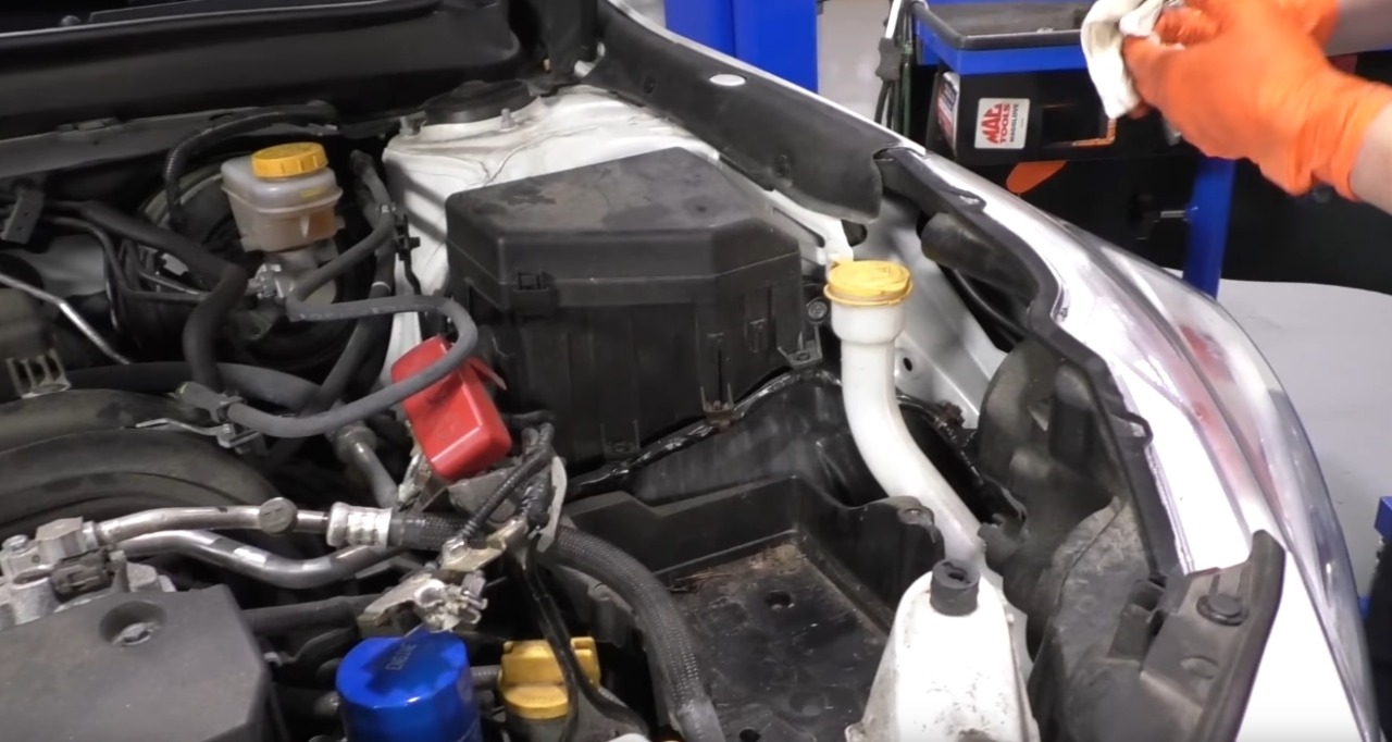 A engine bay of a 2016 subaru outback in a shop, focused on where the battery should be, which only has an empty tray and disconnected terminal connectors