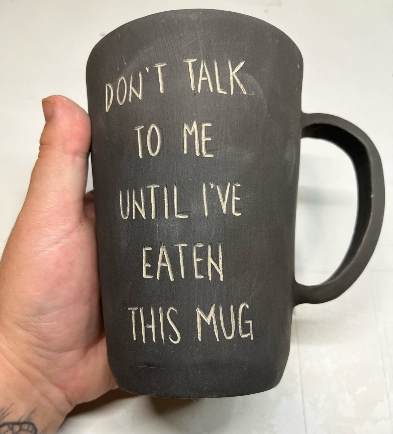 a black greenware mug that reads 'don't talk to me until I've eaten this mug'