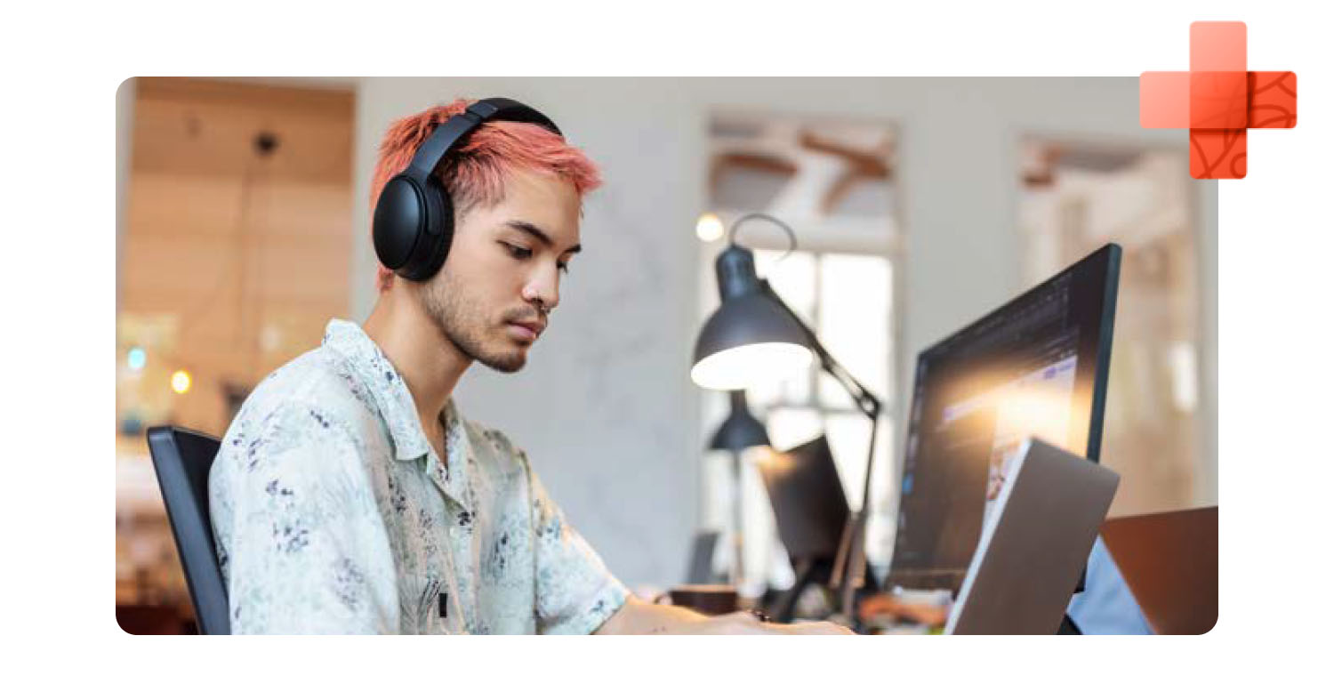 A young man at the office working on his computer with his headphones on.
