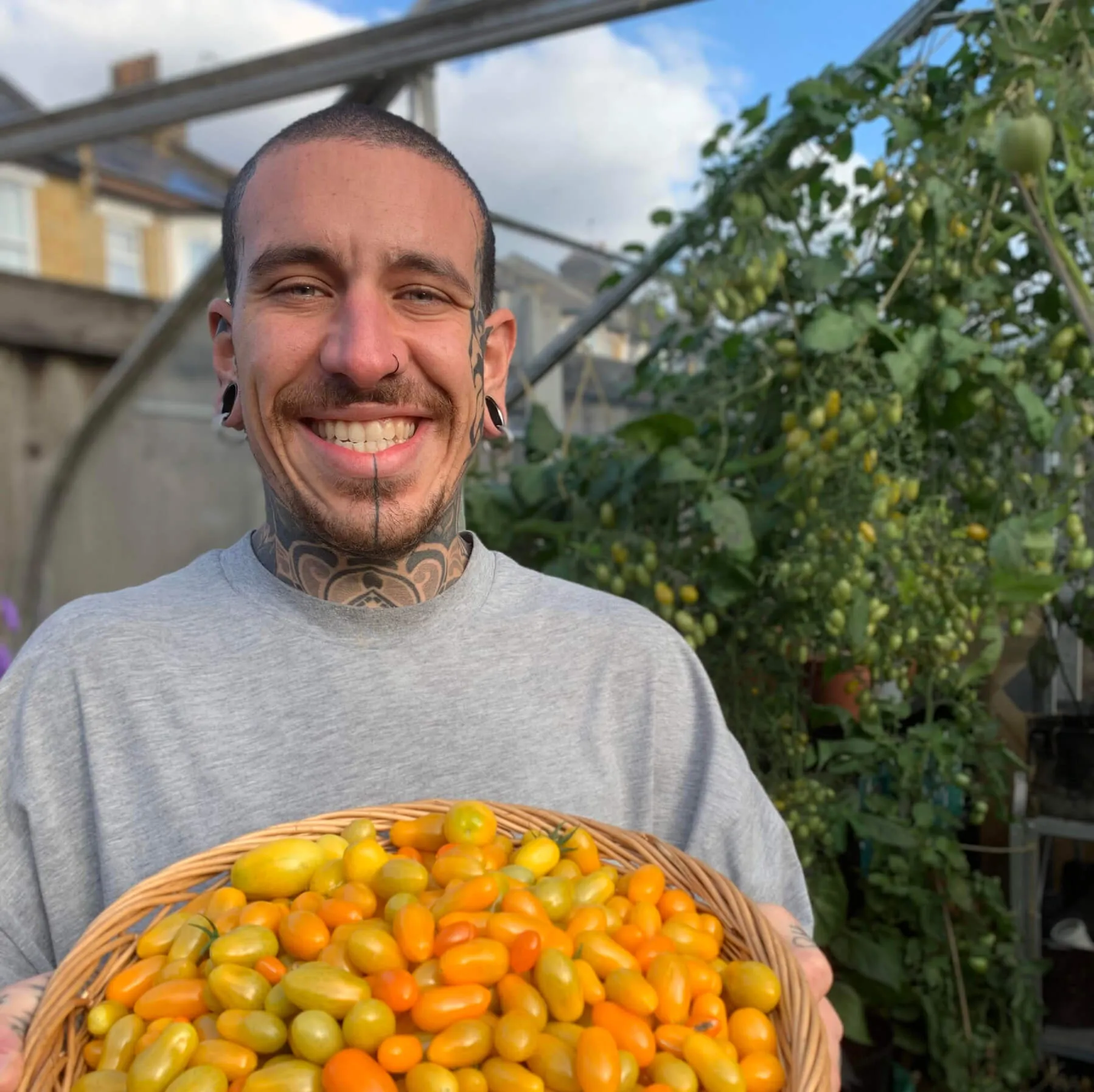 A man smiling and proudly holding a basket of small vegetables to the camera.