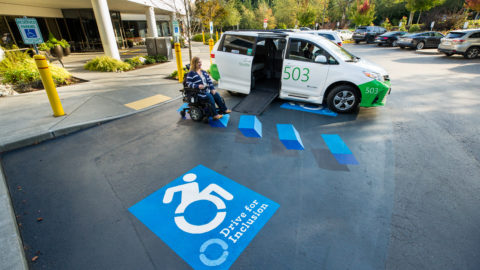 A women in a wheelchair next to a Microsoft shuttle van featuring the new 3-D graphic for ADA Parking spaces at the Living Well Health Center on our Redmond Campus.