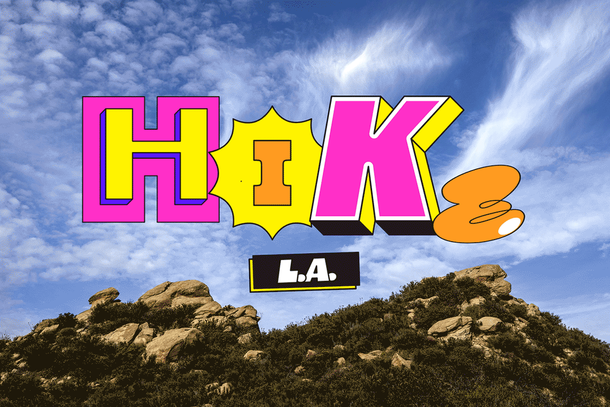 Animated type reading "HIKE L.A." floats against wispy clouds and blue sky above a rocky hilltop.
