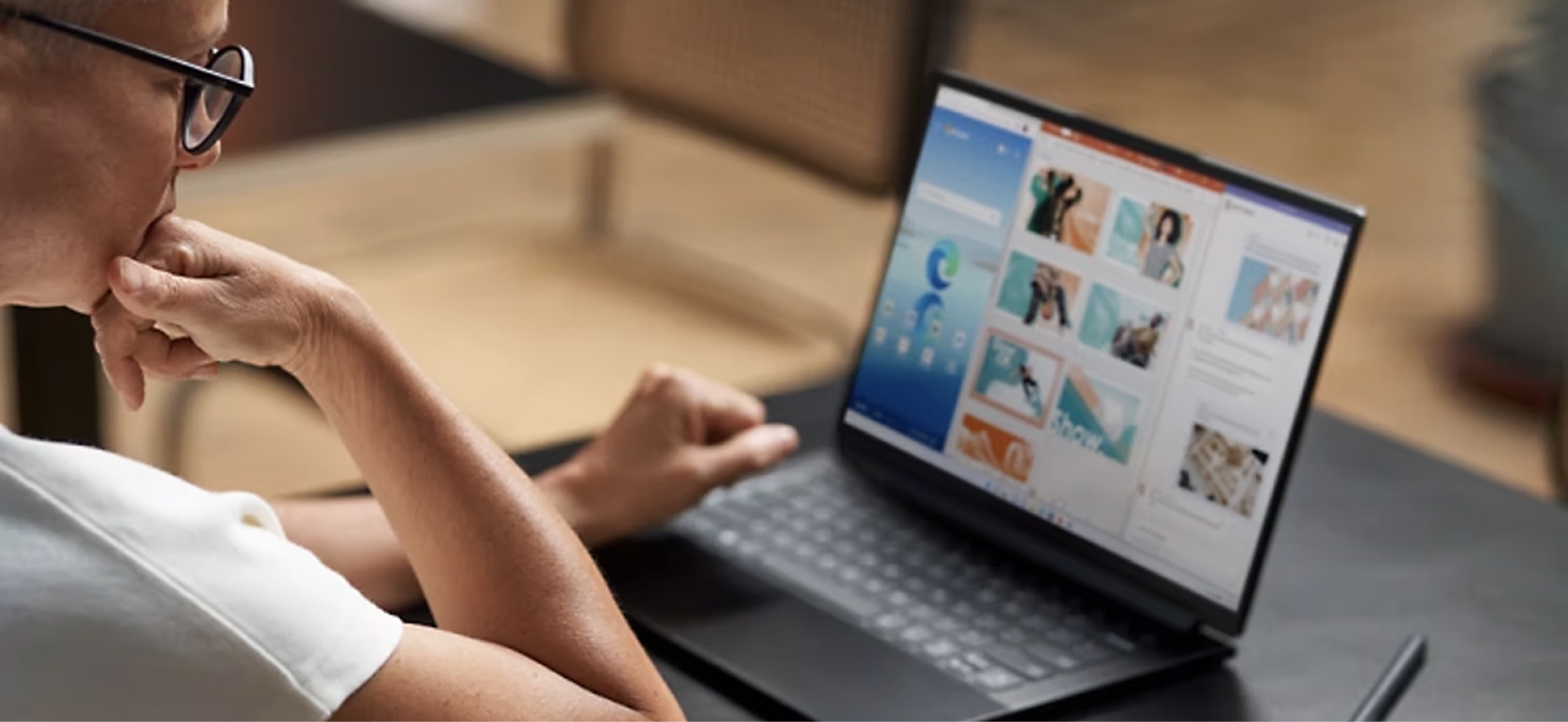Person med briller, der bruger en bærbar computer med farverig hjemmesidegrafik, sidder ved et træbord.