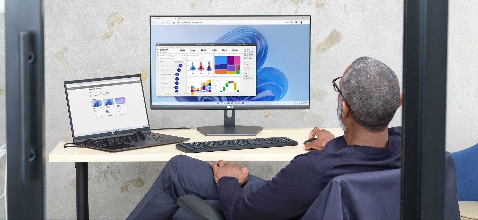 En mand gennemgår datadiagrammer på en computerskærm og en bærbar computer i kontormiljøer.