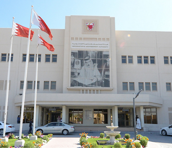 Fasáda budovy informačního a vládního úřadu v Bahrajnu s vlajkami a velkou fotografií hodnostáře