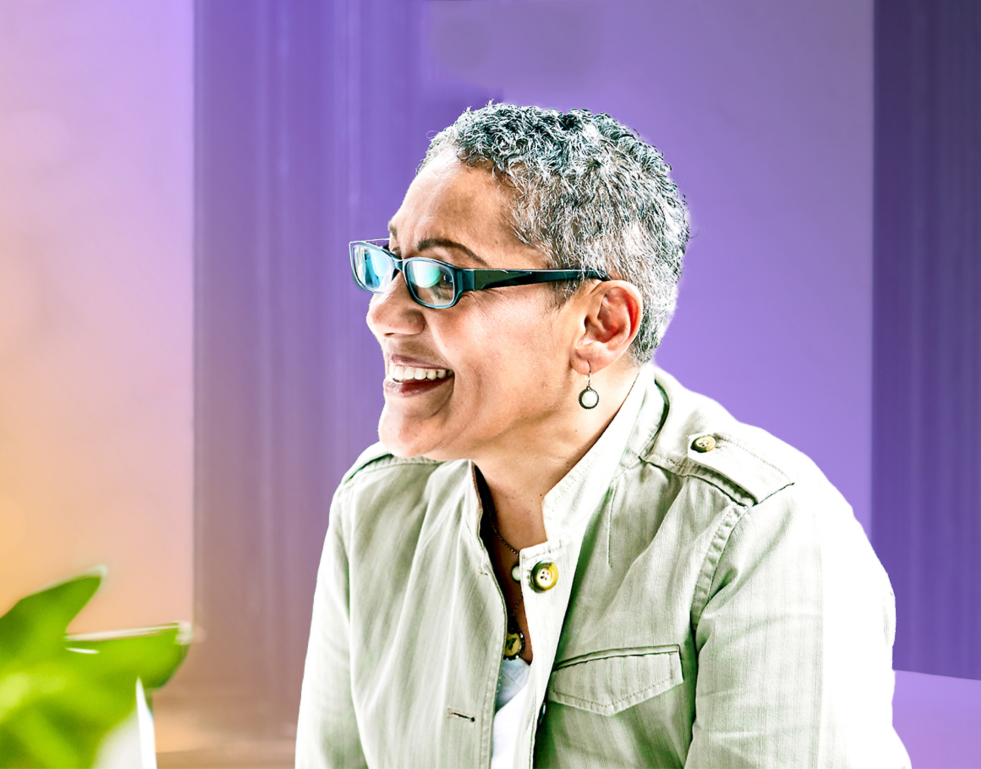 Eine ältere Frau mit kurzen grauen Haaren und Brille in einer hellgrünen Jacke, die lacht. 