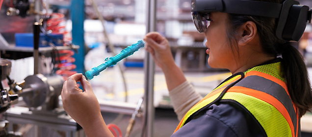Ein Arbeiter, der eine Sicherheitsweste und eine Augmented Reality-Brille trägt, und eine Industriekomponente untersucht.