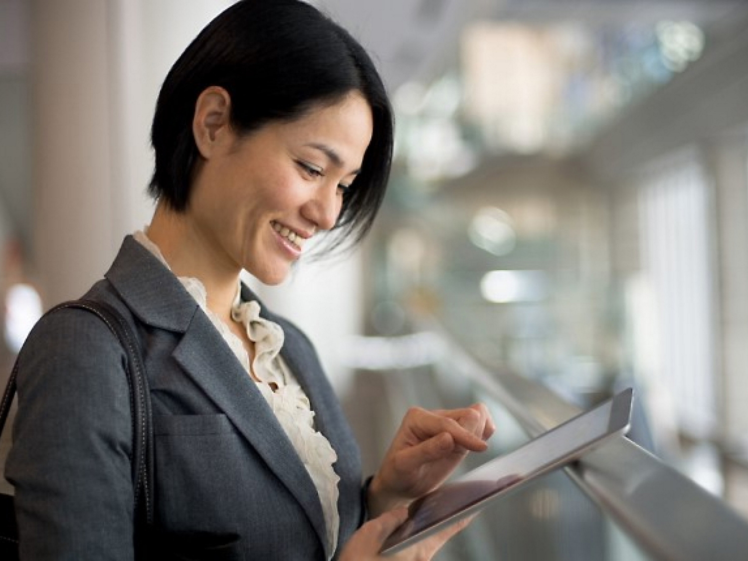 Une femme d'affaires asiatique souriante utilisant une tablette dans un bureau moderne.