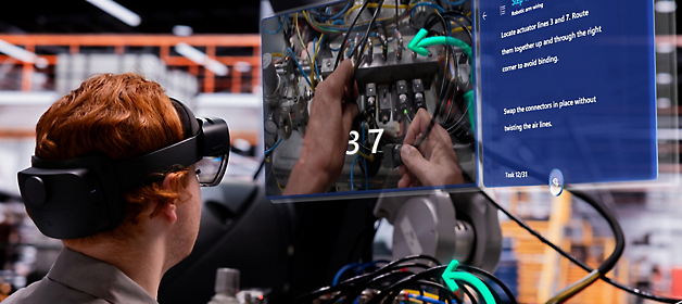Ein Techniker, der ein Virtual Reality-Headset trägt, an einem Elektrischen Panel arbeitet, und auf einen digitalen Overlay-Guide verweist.