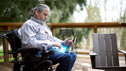 A man who uses a wheelchair works on a laptop while outside.