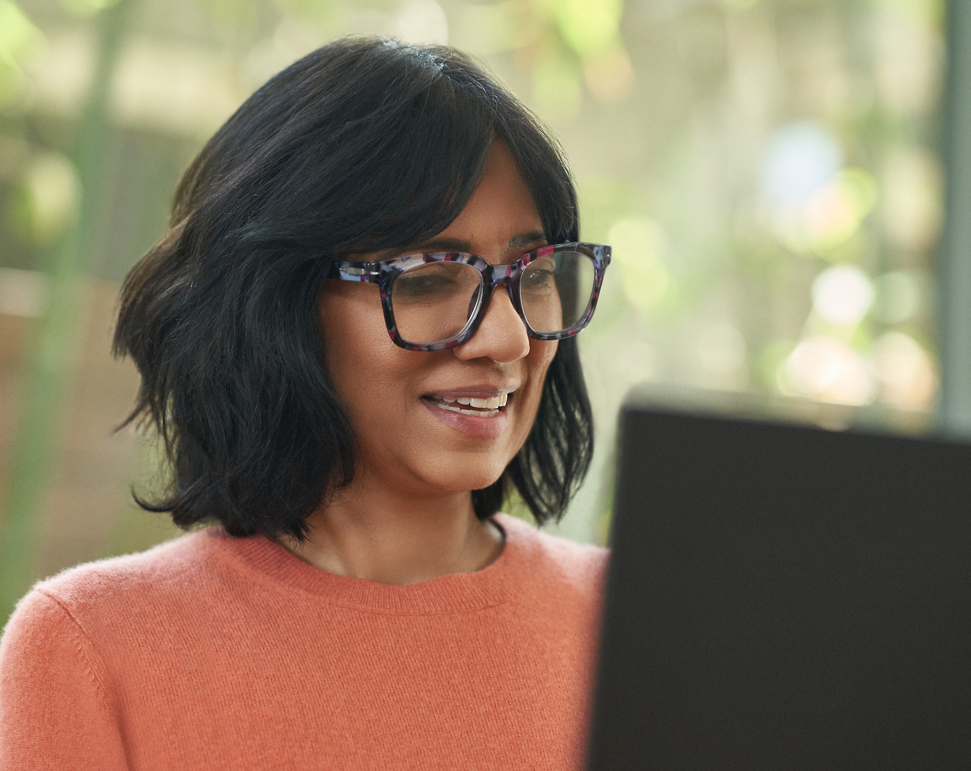 Uma mulher com óculos a sorrir e a trabalhar no seu computador portátil