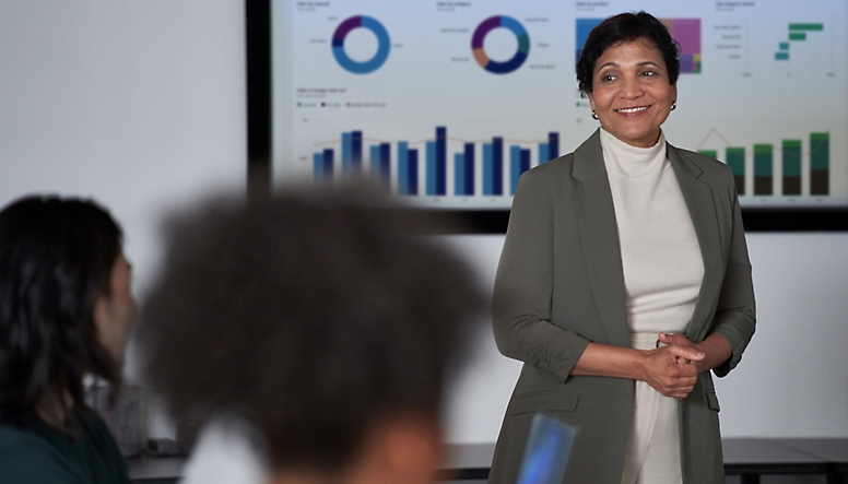 En kvinna i en affärsdräkt står framför en skärm med grafer på sig.