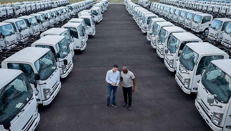 Dois homens em frente a uma fila de camiões brancos.