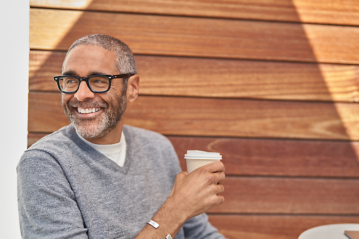 En person som bär glasögon, håller i en kopp och ler.