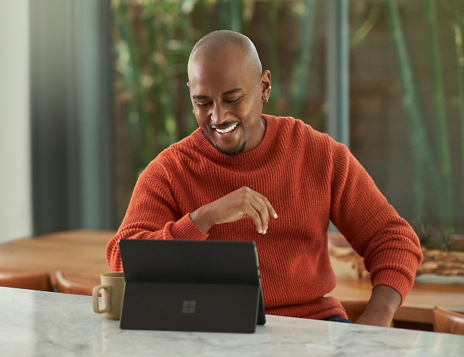 Microsoft Surface Laptop을 가지고 테이블에 앉아 있는 남자입니다.