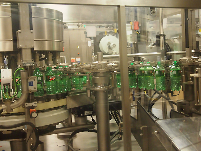 투명한 안전 장벽으로 둘러싸인 자동화된 기계로 녹색 병이 채워지고 뚜껑이 닫히는 병입 공장.