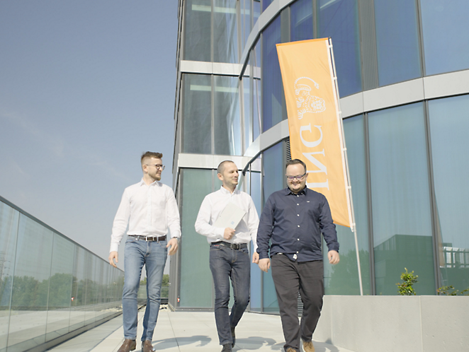 Tre menn som kommer ut av en bygning med et oransje ING-flagg i bakgrunnen 