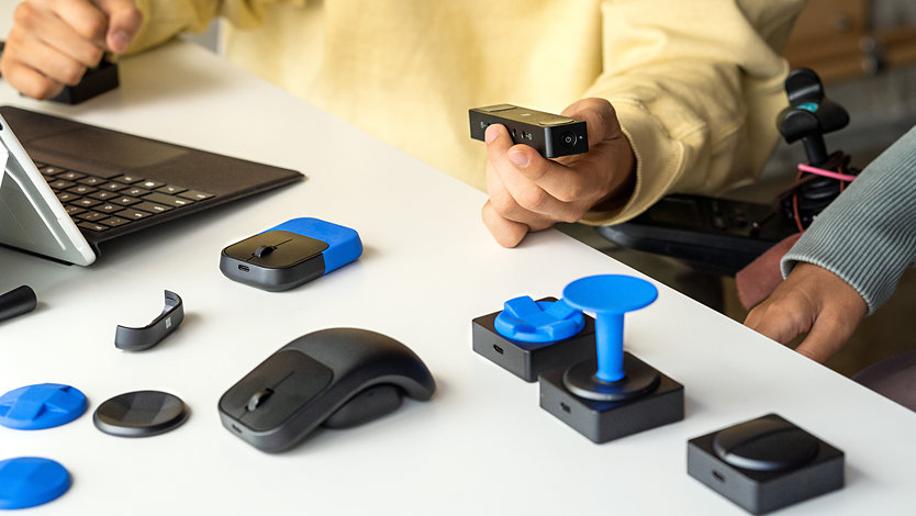 Een persoon gebruikt de Microsoft Adaptive-knop en Microsoft Adaptive-muis met de Microsoft Adaptive Hub in de achtergrond.