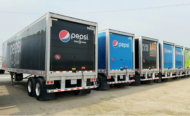 En rad med Pepsi-lastebiler står parkert på en parkeringsplass.