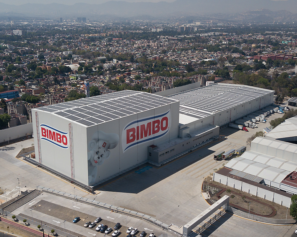 Luchtfoto van een grote Bimbo-bakkerij met magazijnen met logo, omgeven door een stadslandschap.