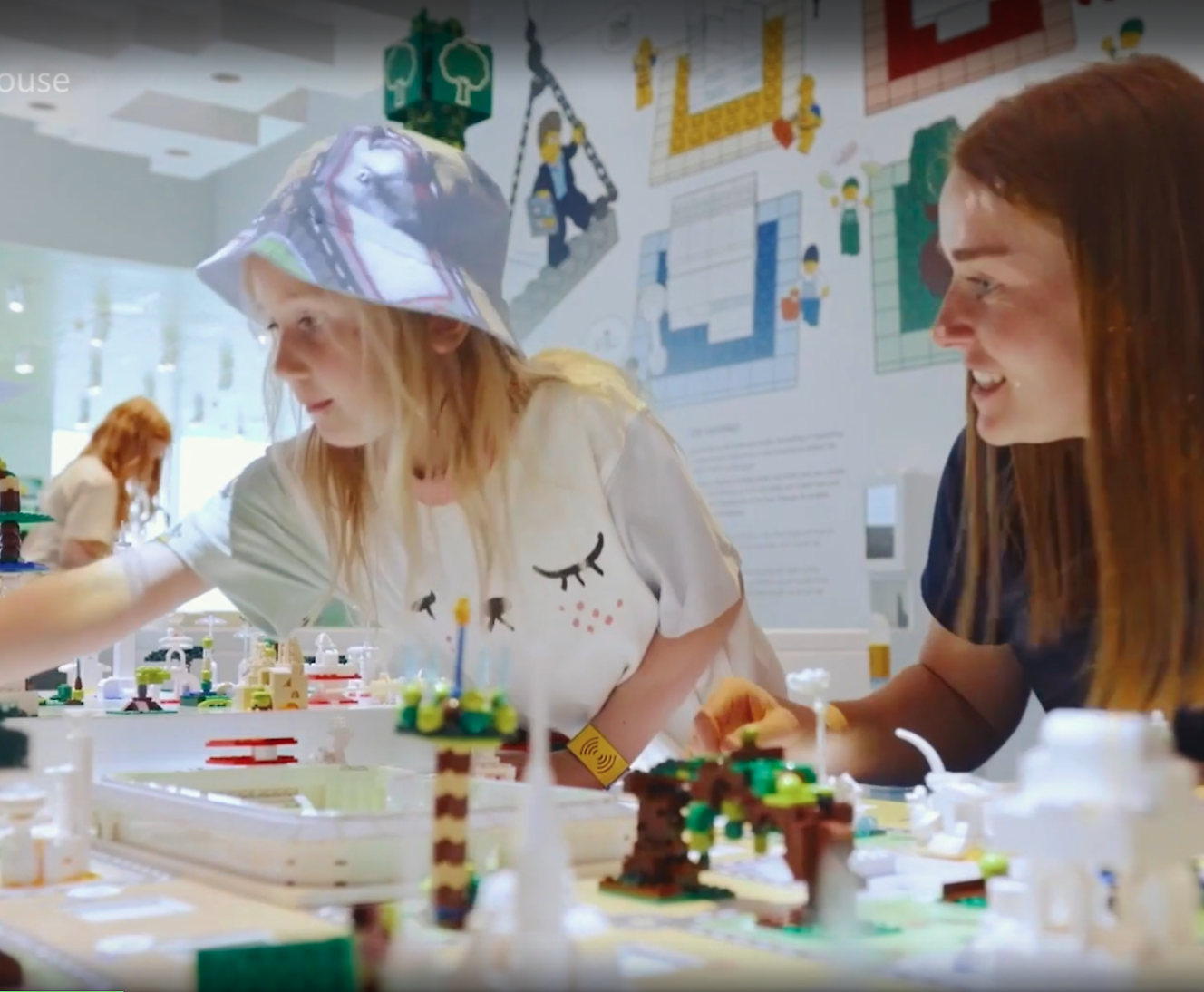 Two women engaging with a lego model at an interactive exhibit, one wearing a face shield.