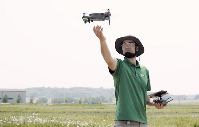 Um homem está a pilotar um drone num campo.