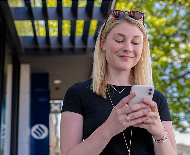 A woman smiling while using her phone with both hands