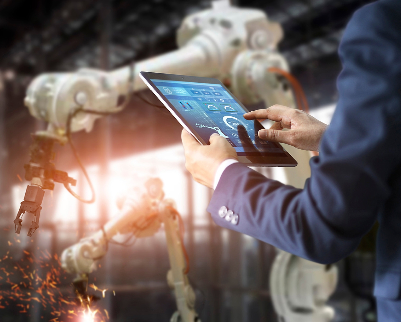 工場にいる人がタブレットを使ってロボット アームを操作し、高度な自動化テクノロジを強調しています。
