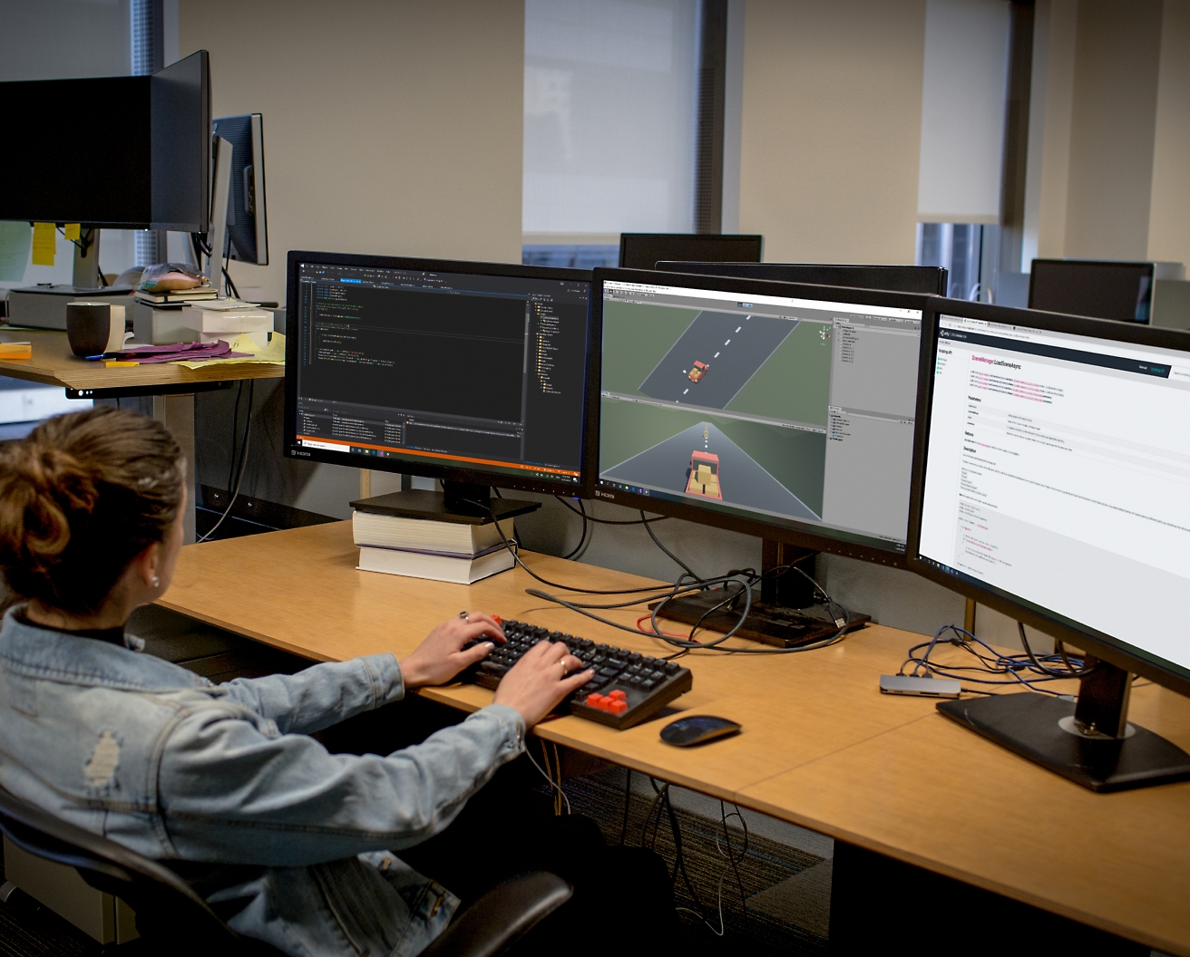 Uma desenvolvedora de software trabalhando em uma configuração com vários monitores em um escritório, programando e depurando software.