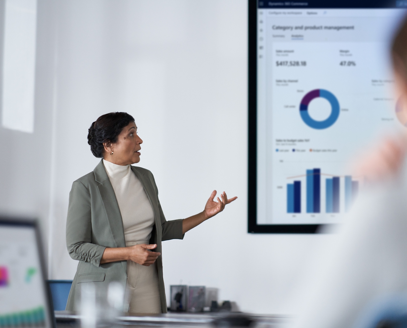 Uma mulher profissional apresenta dados financeiros em uma tela para sua audiência em um ambiente de escritório moderno.
