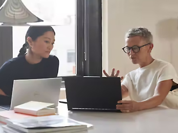 两个人正在坐着看笔记本电脑，并讨论某个主题。