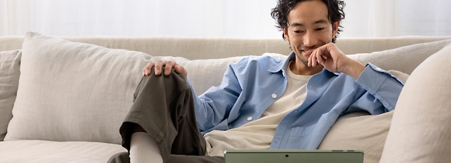 Man sitting on a sofa using a laptop, smiling and looking at the screen.