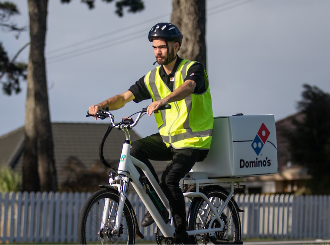 איש משלוחים של Domino's חבוש קסדה ולבוש אפודת בטיחות רוכב על אופניים חשמליים 
