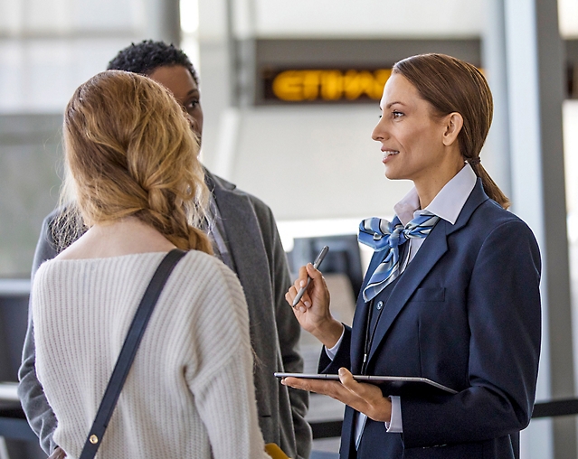 En kvinna i en kostym pratar med en grupp människor på en flygplats.