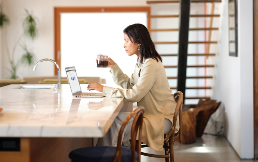 Woman using a Windows 11 computer while drinking coffee in her kitchen.