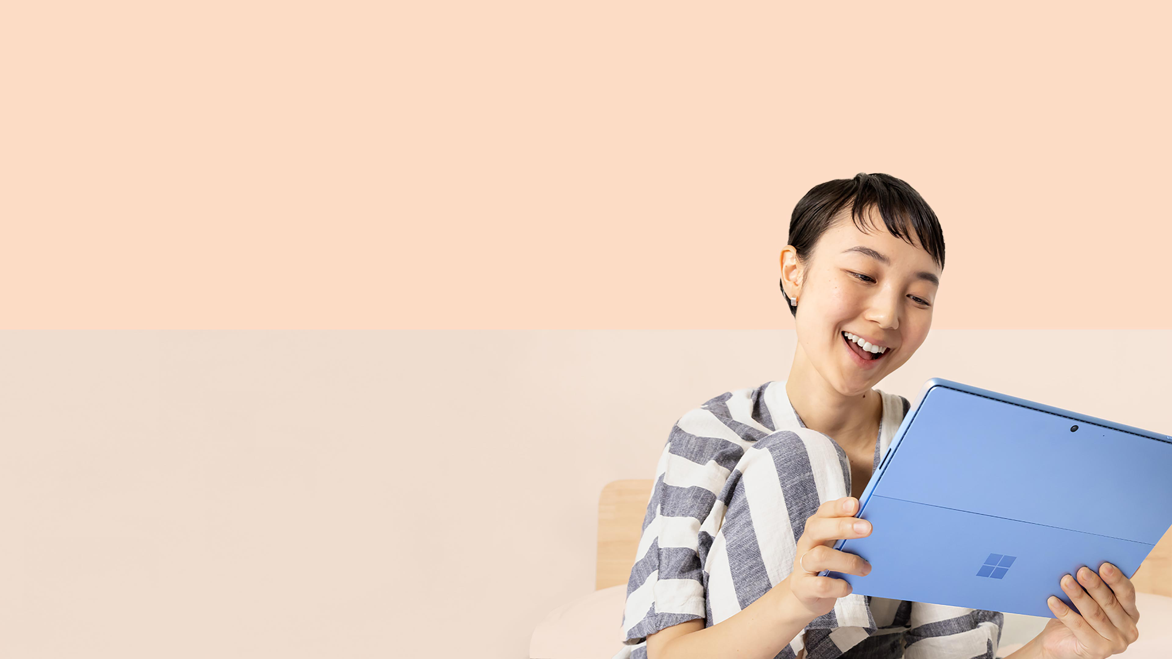 Seorang wanita tersenyum pada Surface Pro 9 miliknya dalam warna Biru Nilam sambil memegang Surface Slim Pen 2.