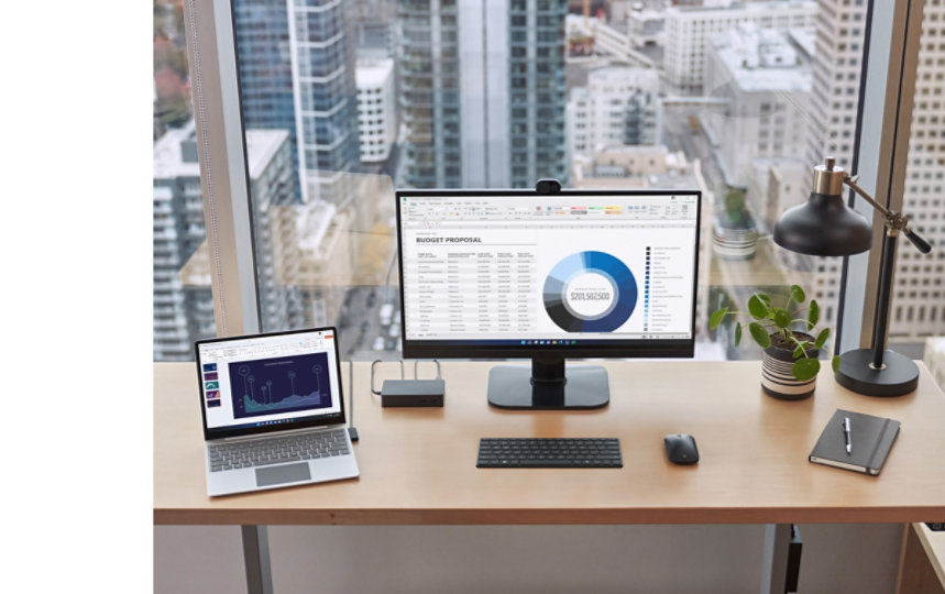 在辦公桌上，一台 Surface 裝置連接到 Surface 擴充基座，附近還有外接螢幕、鍵盤、滑鼠、手寫筆和筆記本