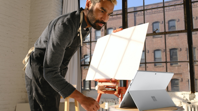 Man looking at Surface device while standing in front of a canvas