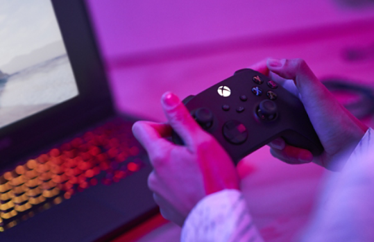 Person holding a gaming controller with laptop in the background