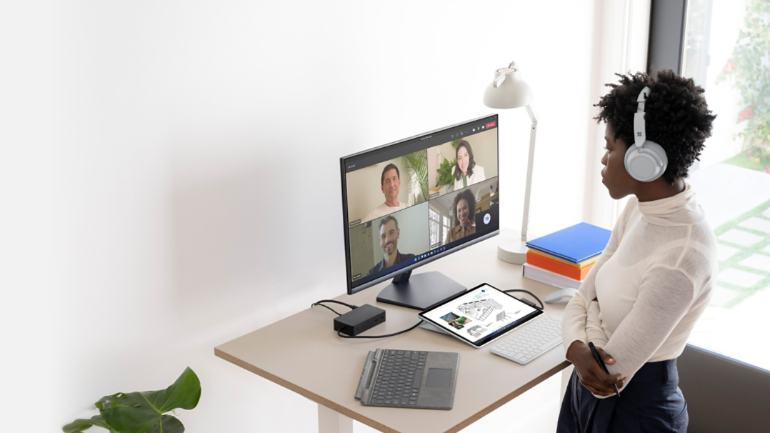 Een persoon staande aan zijn bureau thuis terwijl hij Surface Pro 8 en meerdere Surface-accessoires gebruikt