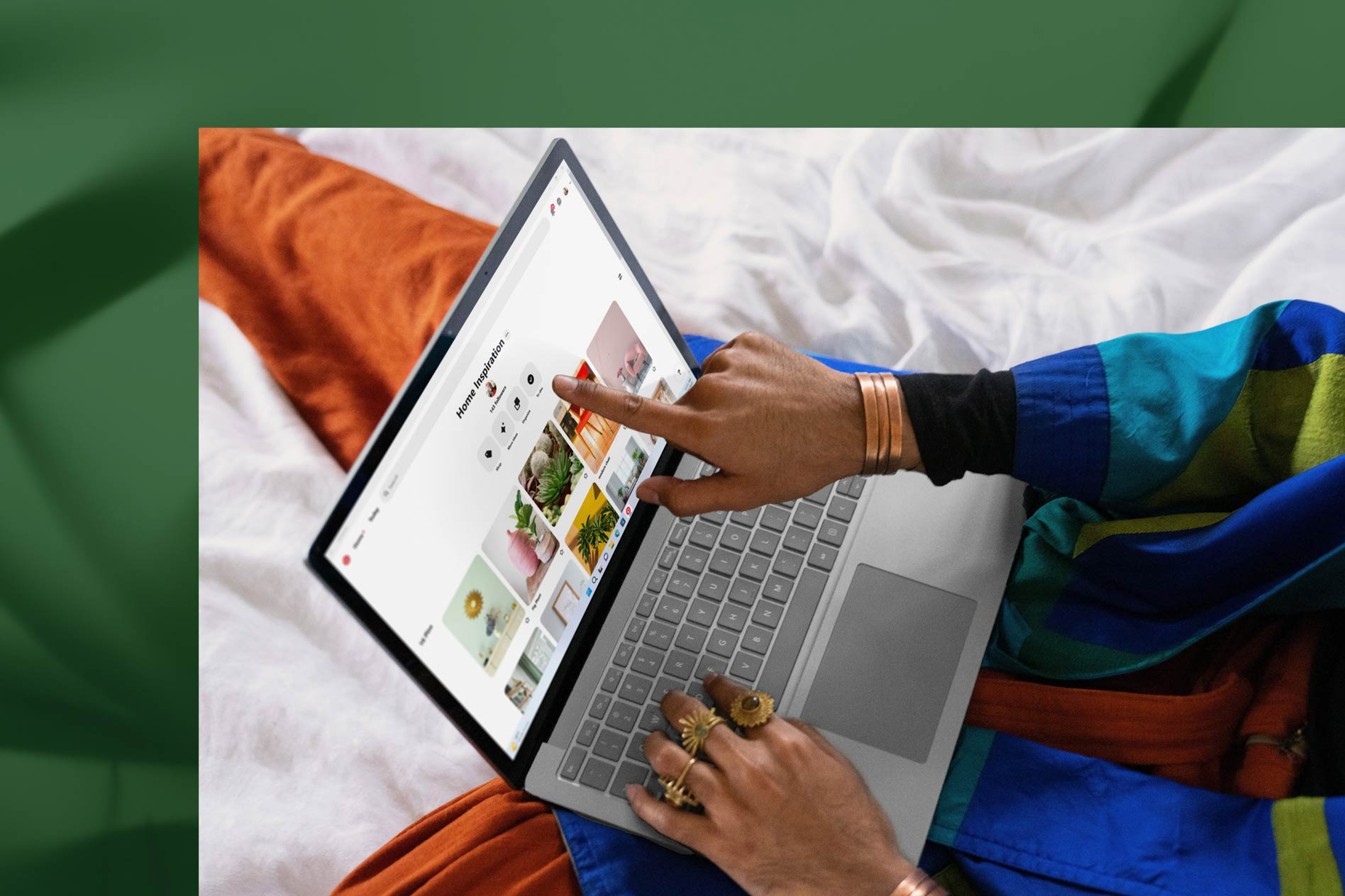 Seseorang menyentuh skrin Surface Laptop 5 berwarna Platinum miliknya sambil bekerja di atas katil.