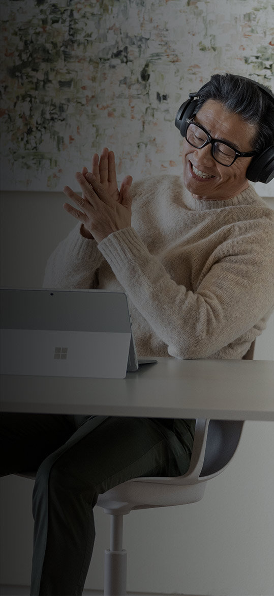 رجل يجلس في مكتبه بالمنزل مستمتعًا بجهازه Surface Pro 9‎ أثناء ارتداء سماعات الرأس Surface Headphones 2+‎
