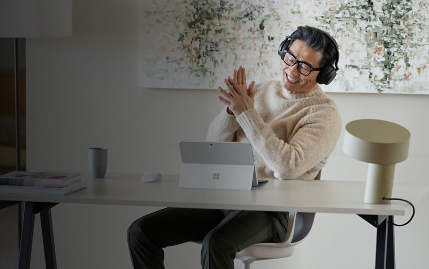 رجل يجلس في مكتبه بالمنزل مستمتعًا بجهازه Surface Pro 9‎ أثناء ارتداء سماعات الرأس Surface Headphones 2+‎