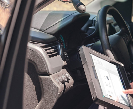A policewoman is seen sitting in the passenger seat of her cruiser while using a Surface Pro device