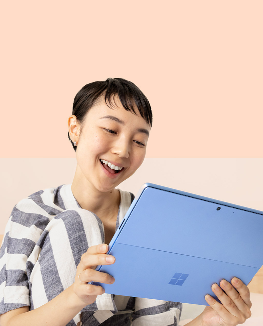 Seorang wanita tersenyum pada Surface Pro 9 miliknya dalam warna Biru Nilam sambil memegang Surface Slim Pen 2.