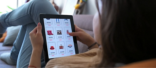 침대에 누워 태블릿으로 쇼핑 웹사이트를 보고 있는 한 소녀.